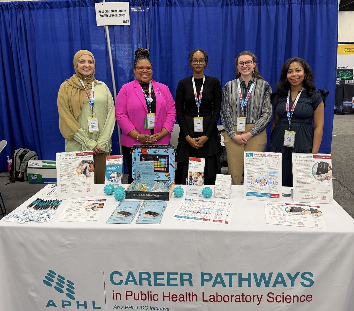 The Academic Partnerships team pose behind an APHL table at a career fair.